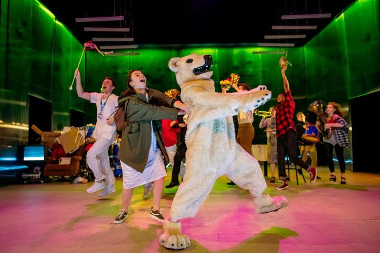 Actor in a polar bear costume dancing on stage with other actors
